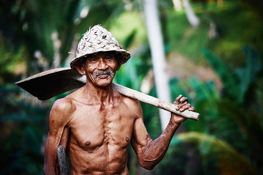 A vital elder farmer carrying his tools, reflecting a life rooted in nature and movement
